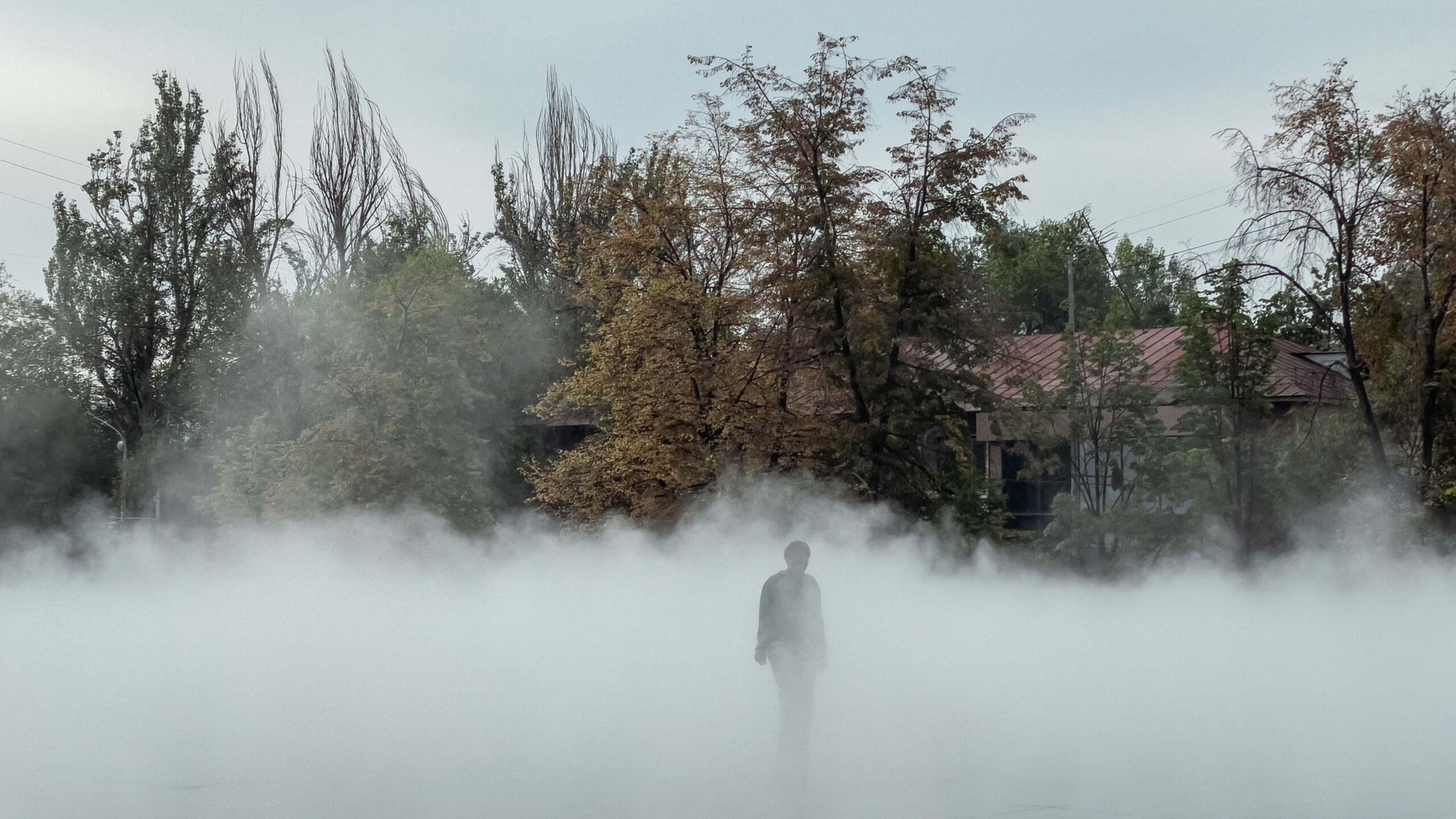 A human silhouette is seen walking through fog, in front of a wooded area, in Almaty, Kazakhstan.